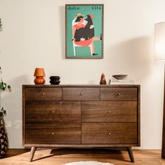 a wooden dresser sitting in a living room next to a wall with a poster on it