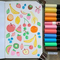 an open notebook with fruit and vegetables drawn on it next to crayon markers