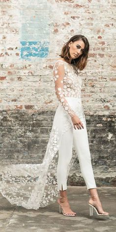 a woman in white is standing near a brick wall and wearing high heeled sandals