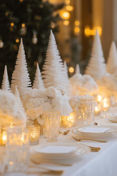 the table is set with candles, plates and vases filled with white flowers in front of a christmas tree