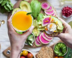 two people holding up sandwiches with fruit and veggies in the background