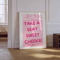 a pink poster with the words take a seat, sweet cheeks on it in front of a white wall