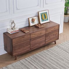 a sideboard with two pictures on it in front of a white wall and rug