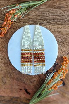 two beaded earrings sitting on top of a white plate next to some dried flowers