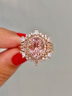 a woman's hand holding an engagement ring with a pink diamond in the center