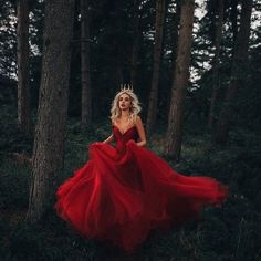 a woman in a red dress is walking through the woods