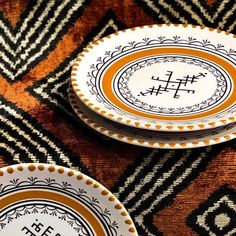 two white and orange plates sitting on top of a patterned table cloth with black letters