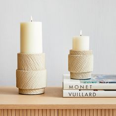 two white candles sitting on top of a wooden table next to a stack of books