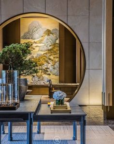 a table with vases and plants on it in front of a wall hanging painting