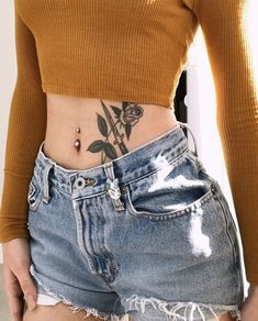 a woman with a rose tattoo on her stomach wearing denim shorts and a brown sweater