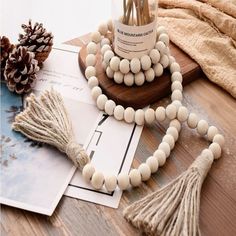 a wooden beaded necklace with tassels sits on a table next to pine cones