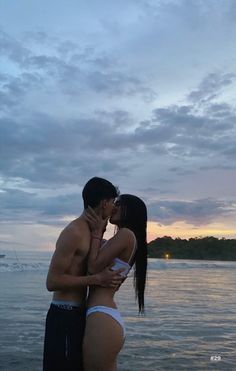 a man and woman kissing in front of the ocean at sunset or dawn with clouds above them