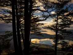 the sun is setting behind some trees on top of a hill with water in the distance