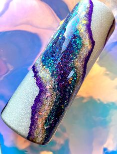 a purple, blue and white marble with glitter on it's side is shown in front of a multicolored background