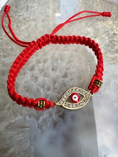 a red string bracelet with an evil eye on it and a gold plated charm