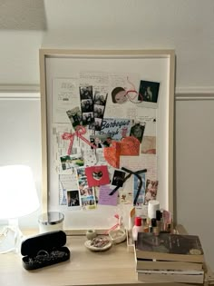 a desk topped with lots of clutter next to a lamp and pictures on the wall