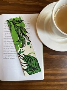 a bookmark with green leaves on it next to a cup of coffee and saucer