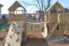 a wooden play set in the middle of a yard with two children playing on it