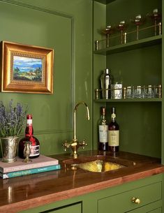 a kitchen with green painted walls and wooden counter tops, gold faucet, brass sink, wine glasses on shelves