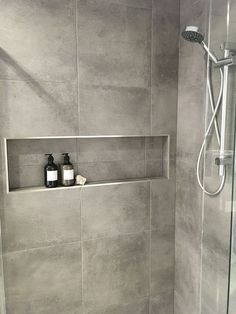 a bathroom with a glass shower door and gray tile walls, along with two bottles on the shelf