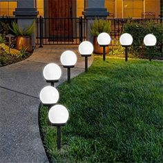 several lights that are on the ground in front of a house with grass and bushes