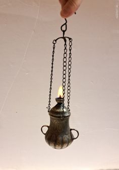 a hand holding a small metal teapot with a candle in it