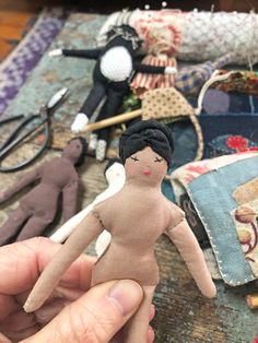 a hand holding a doll in front of some sewing supplies on a wooden table with scissors and thread