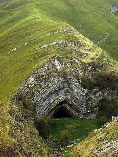 an open hole in the side of a mountain with grass growing on it's sides