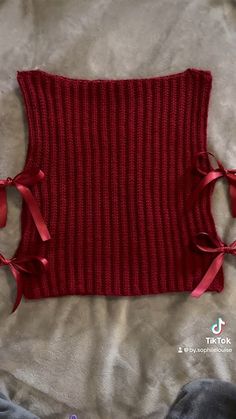 a red knitted sweater with bows on the front and back, sitting on a bed