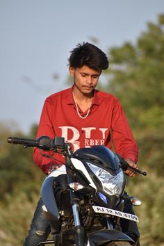 a man sitting on top of a motorcycle in front of some bushes and trees with his hand on the handlebars