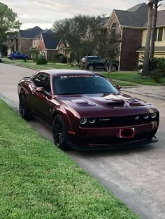 a red sports car parked on the side of a road next to grass and houses