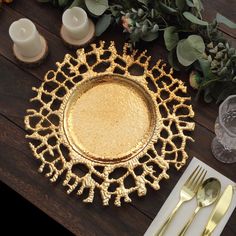 a gold plate sitting on top of a wooden table next to silverware and candles