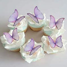 several cupcakes with purple butterflies on them sitting in a circle, surrounded by white frosting