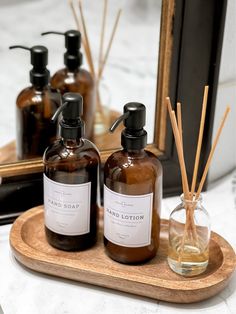 three bottles of soap and reeds on a wooden tray in front of a mirror