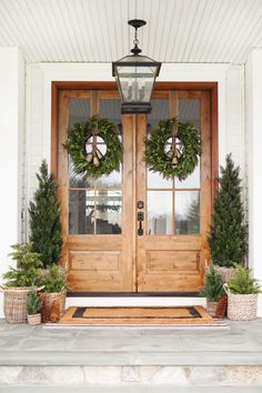 two wreaths on the front door of a house with potted plants in front