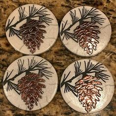 four ceramic pinecone coasters with copper leaf designs on white marble counter top