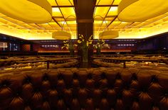 the interior of a restaurant with leather couches and yellow lights on the ceiling above