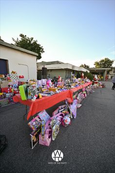 a long table with many items on it in the middle of a parking lot next to some houses