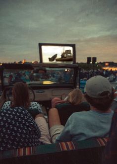 three people sitting in the back of a truck watching a movie