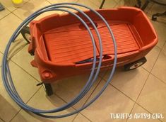 an orange plastic wagon with blue hoses on the floor in front of a tile floor