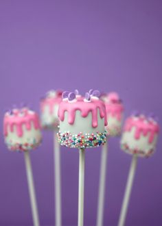 cake pops with pink frosting and sprinkles on top, sitting in front of a purple background