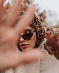 a woman wearing sunglasses and a leopard print head scarf is making the hand gesture with her fingers