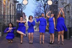 four women in blue dresses are posing for a photo on a brick sidewalk with their hands up