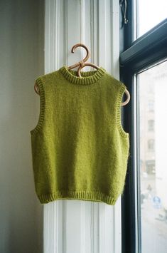 a green knitted sweater hanging on a window sill next to a wooden hanger