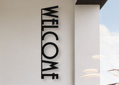 a welcome sign is mounted on the side of a white building with black lettering that reads welcome