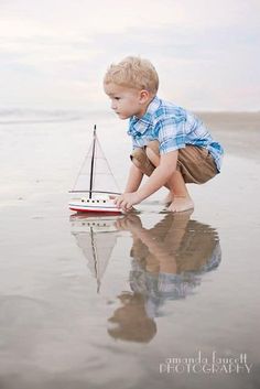 a little boy playing with a toy boat on the beach