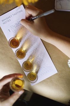 a person writing on a piece of paper next to some glasses with liquid in them