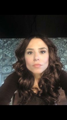 a woman with long brown hair sitting in front of a mirror looking at the camera