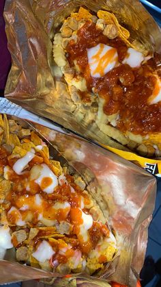 two pizzas covered in sauce and cheese sitting on top of foil wrappers next to each other