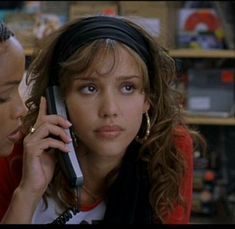 two women are talking on cell phones in a room with bookshelves and shelves